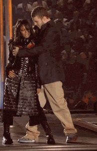 An animated GIF: Justin Timberlake and Janet Jackson perform on stage during the half-time show, standing close together as Timberlake reaches across the Janet's chest, and pulls the right breast cup off Janet's costume. The scene appears to be in front of a large audience.